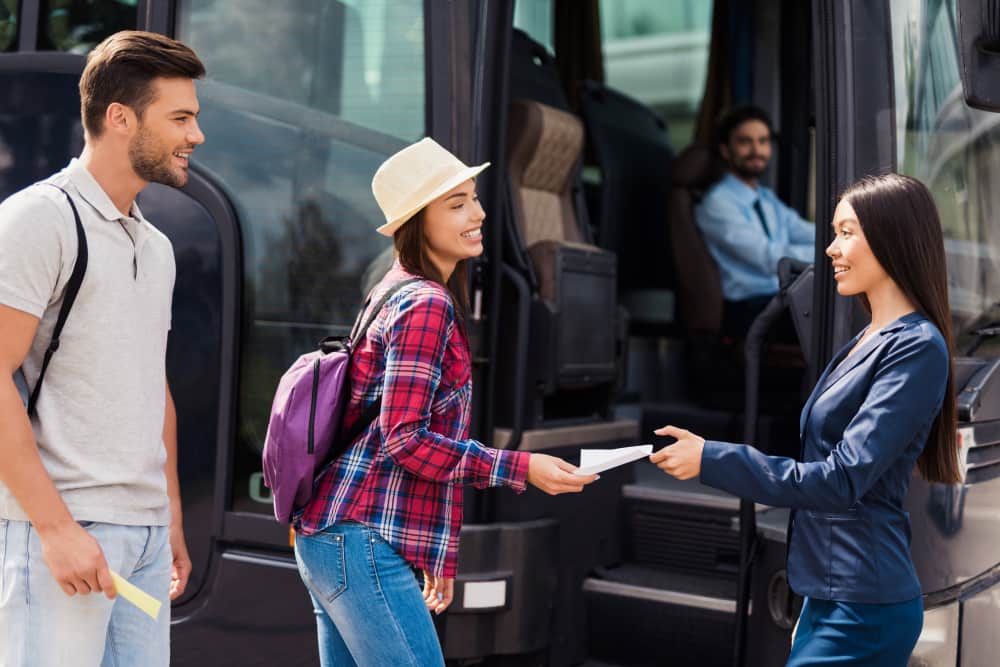 Une hôtesse accueille avec le sourire des voyageurs munis de billets pour leur expliquer comment bien organiser son transport de groupe en autocar.