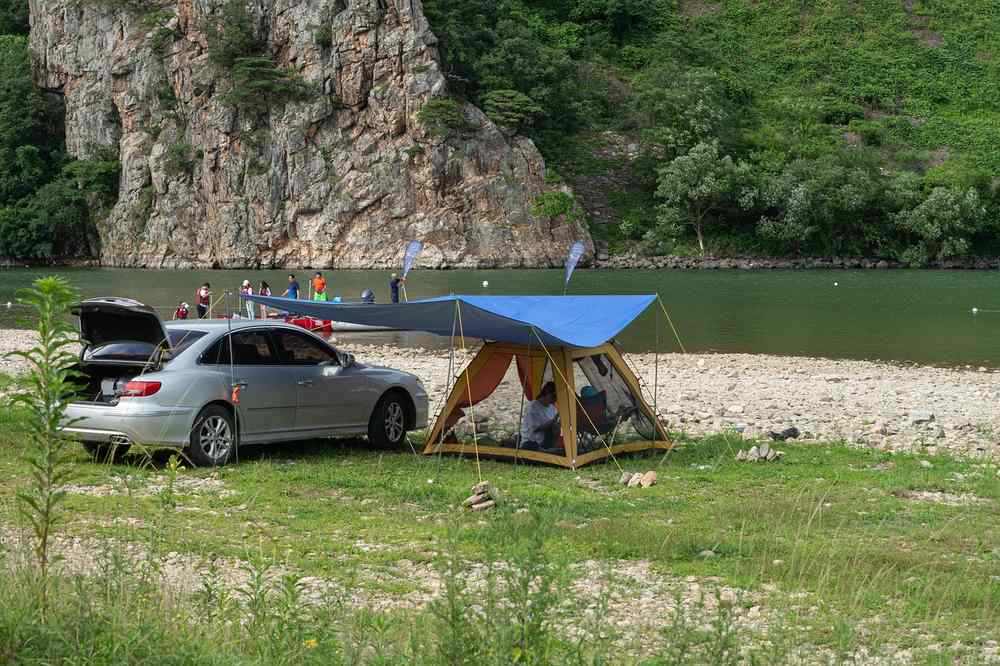 Camping aménagé au bord d'une rivière avec voiture et tente bleue