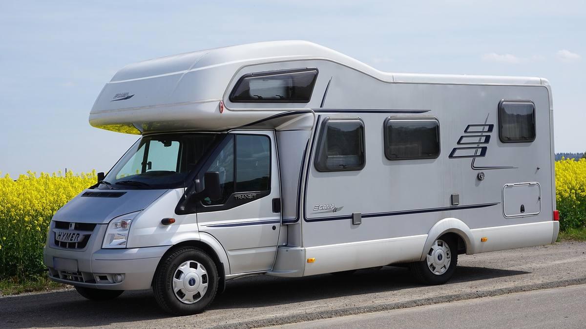 Camping-car de classe moyenne stationné au bord d'une route, paysage agricole avec champ de colza en arrière-plan