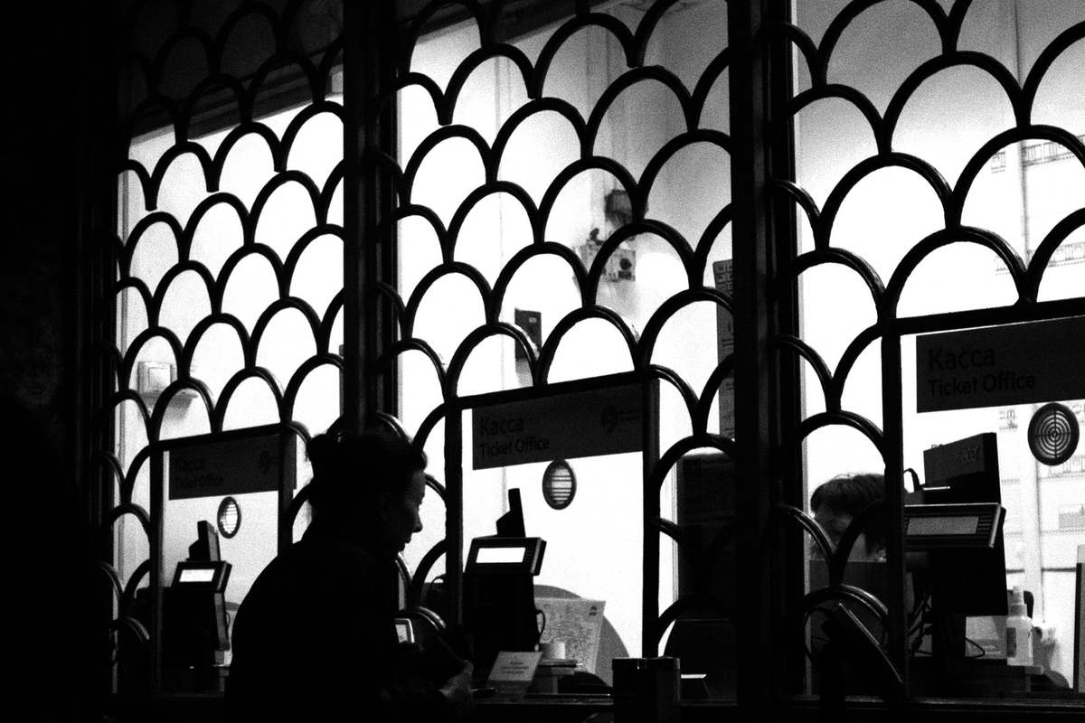 Silhouette d'une personne devant une borne informatique, à travers une fenêtre avec motifs en arc