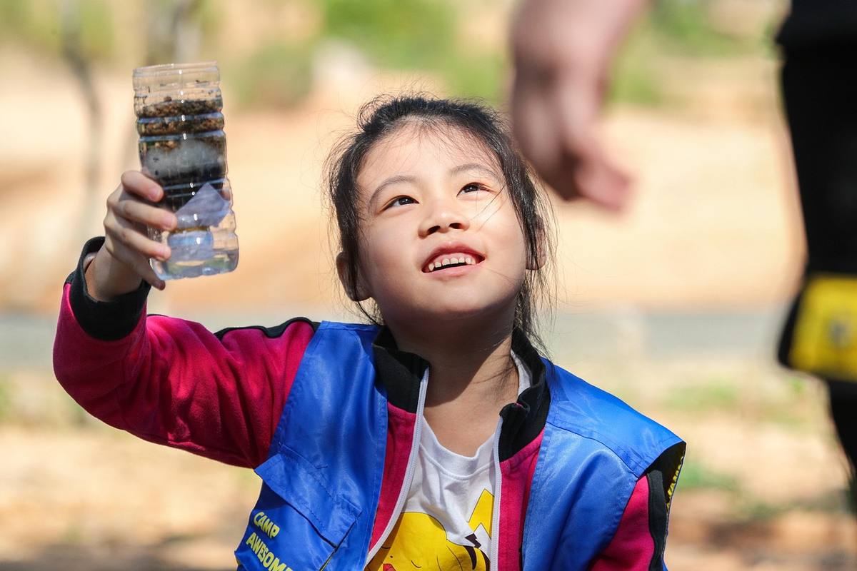 Jeune enfant tenant un verre d'eau transparent en plein air, vêtu d'une veste colorée