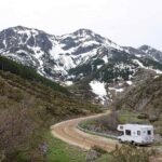 Une caravane suit une route courbée au pied des montagnes enneigées