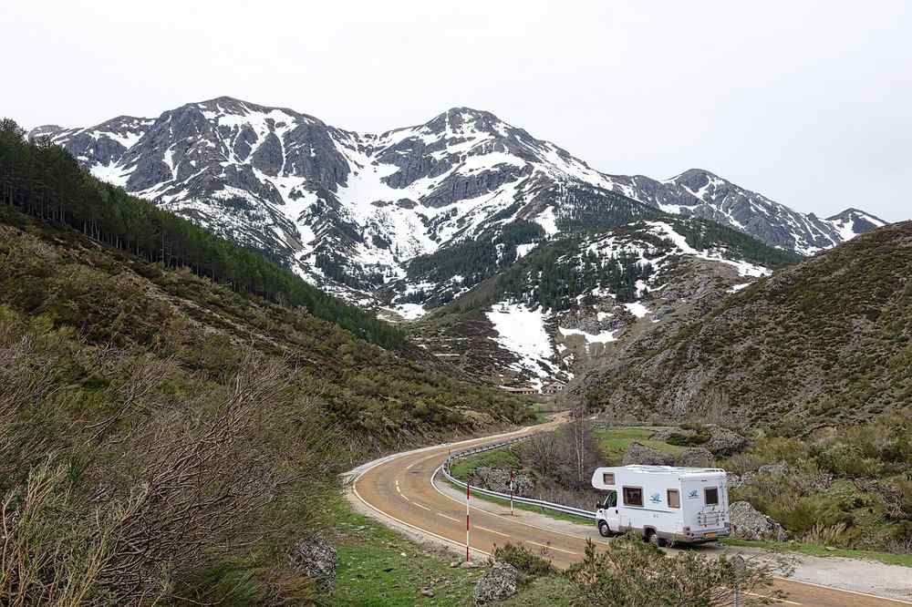 Une caravane suit une route courbée au pied des montagnes enneigées