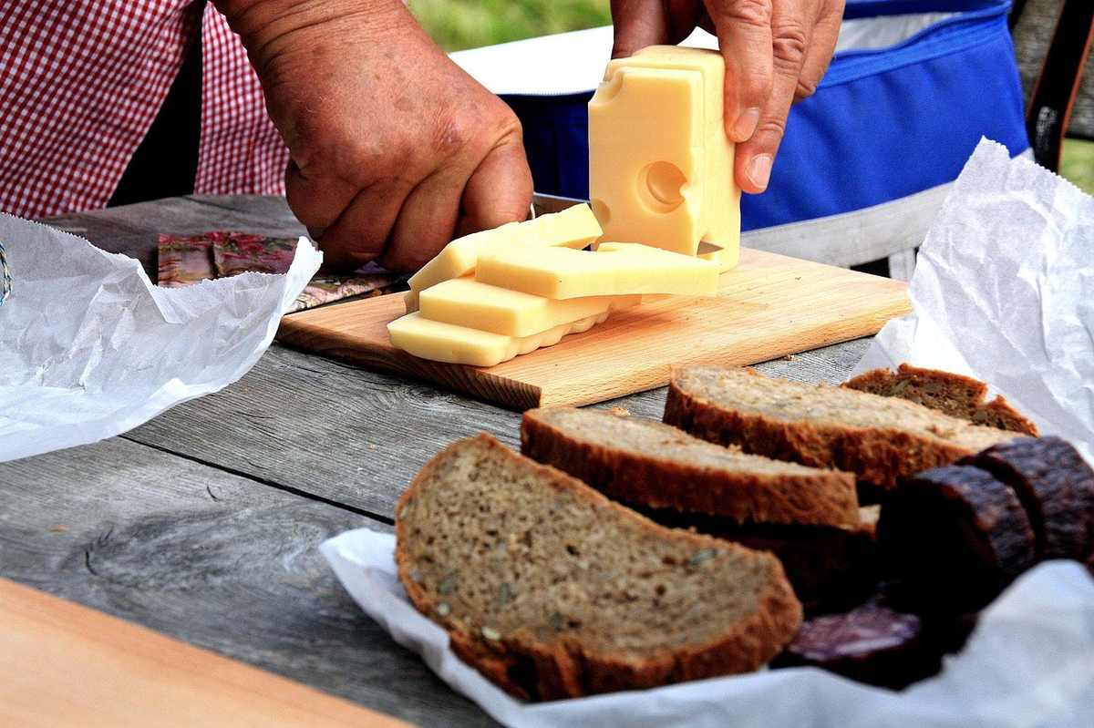 Mains coupant du fromage, pain et viande sur une table en bois Mains coupant du fromage, pain et viande sur une table en bois