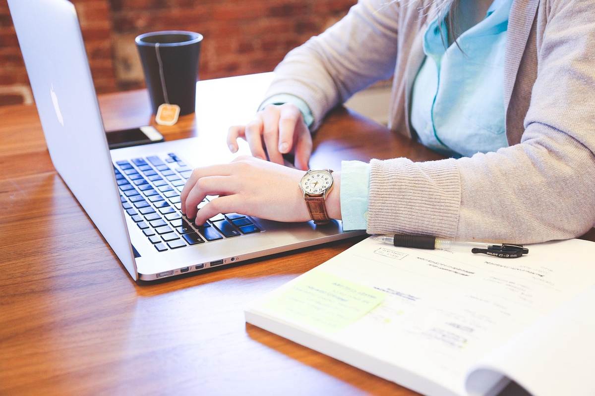 Une femme tape sur un clavier d'ordinateur portable à son bureau en bois, avec un café à proximité Une femme tape sur un clavier d'ordinateur portable à son bureau en bois, avec un café à proximité