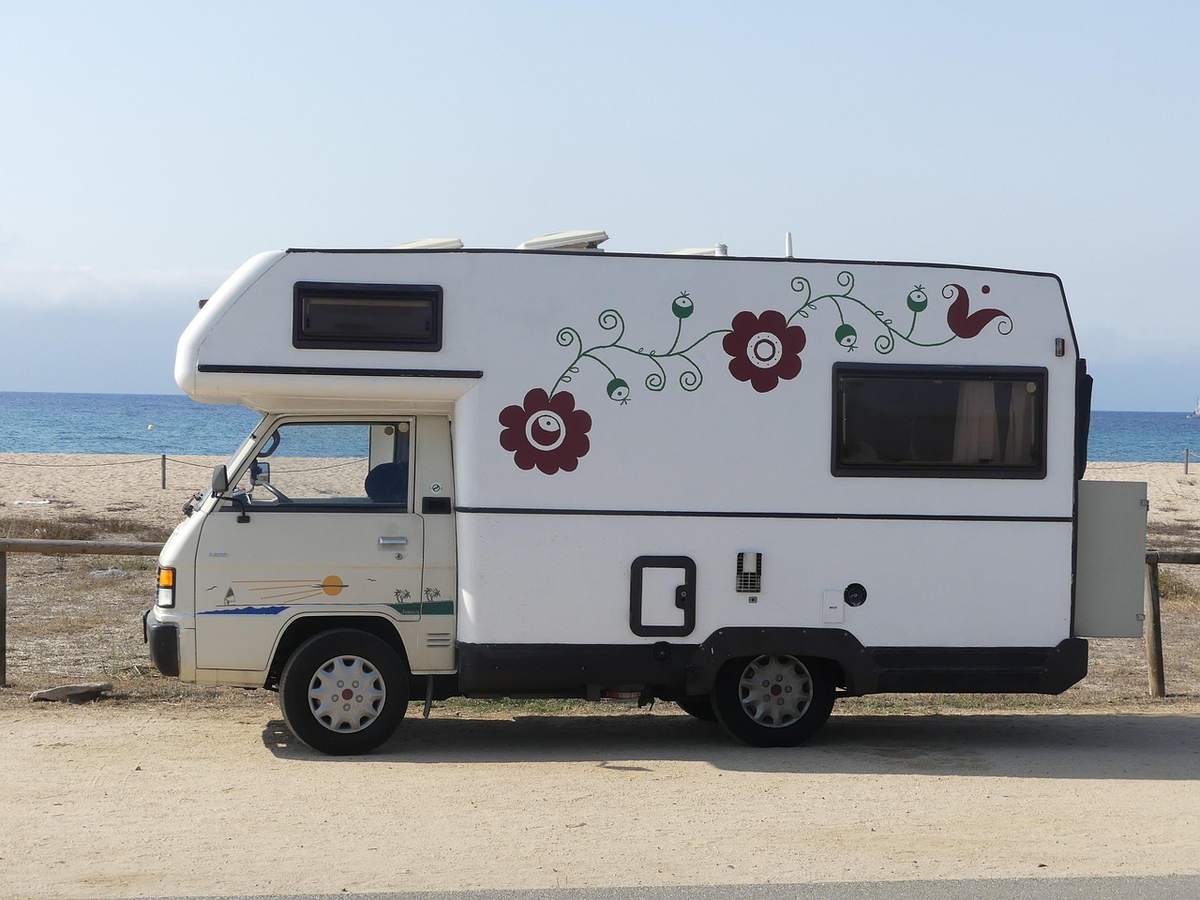 Camion‑caravane blanche avec fleurs rouges et oiseau, stationnée sur sable