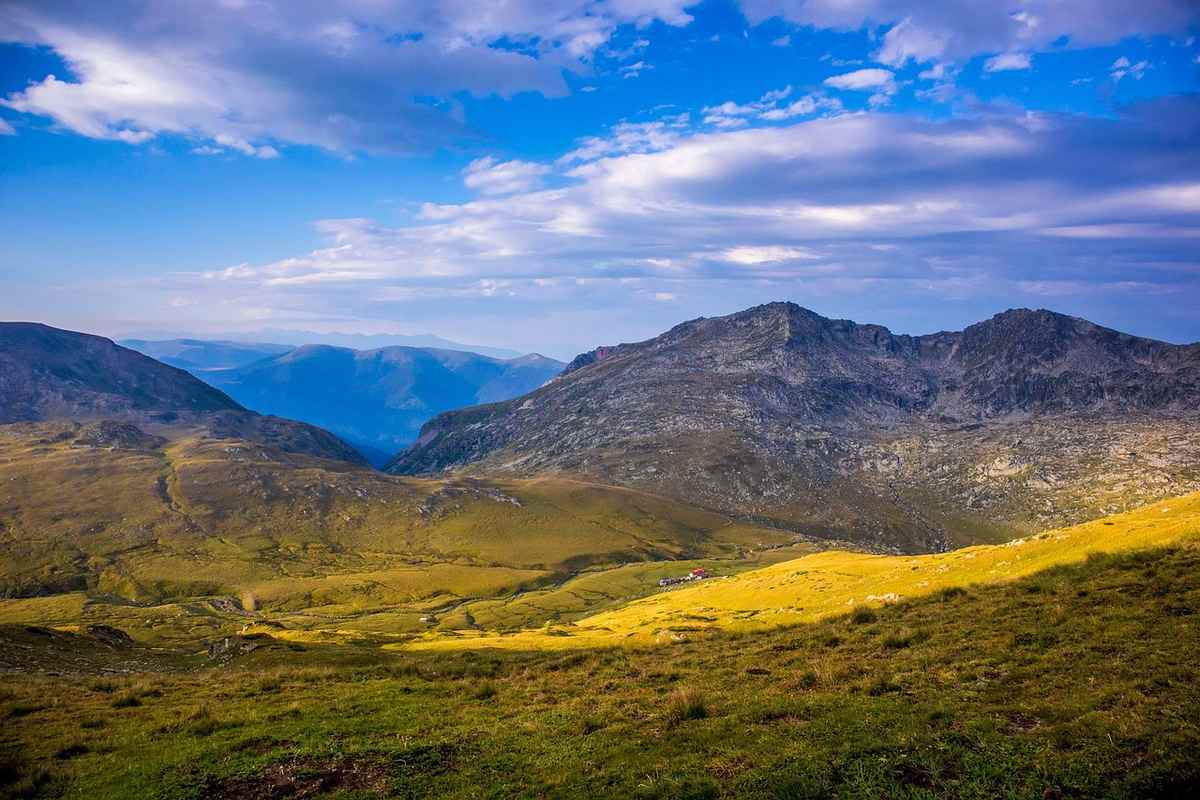 Paysage montagneux avec vallées verdoyantes sous ciel bleu nuageux