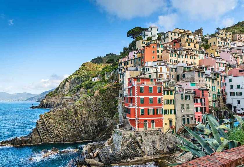 Village aux maisons colorées imbriquées sur falaise rocheuse dominant la mer Méditerranée bleue