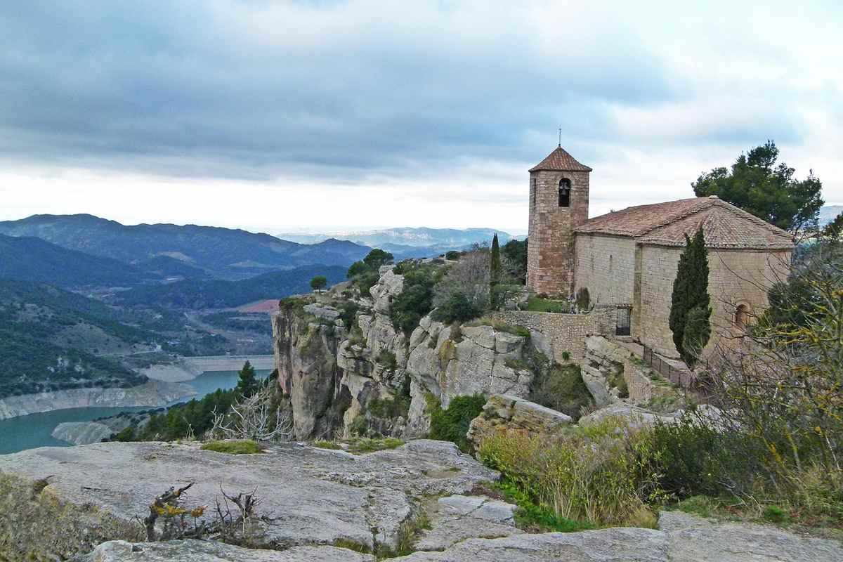 Église perchée sur une falaise avec vue sur une vallée et un ciel nuageux Église perchée sur une falaise avec vue sur une vallée et un ciel nuageux