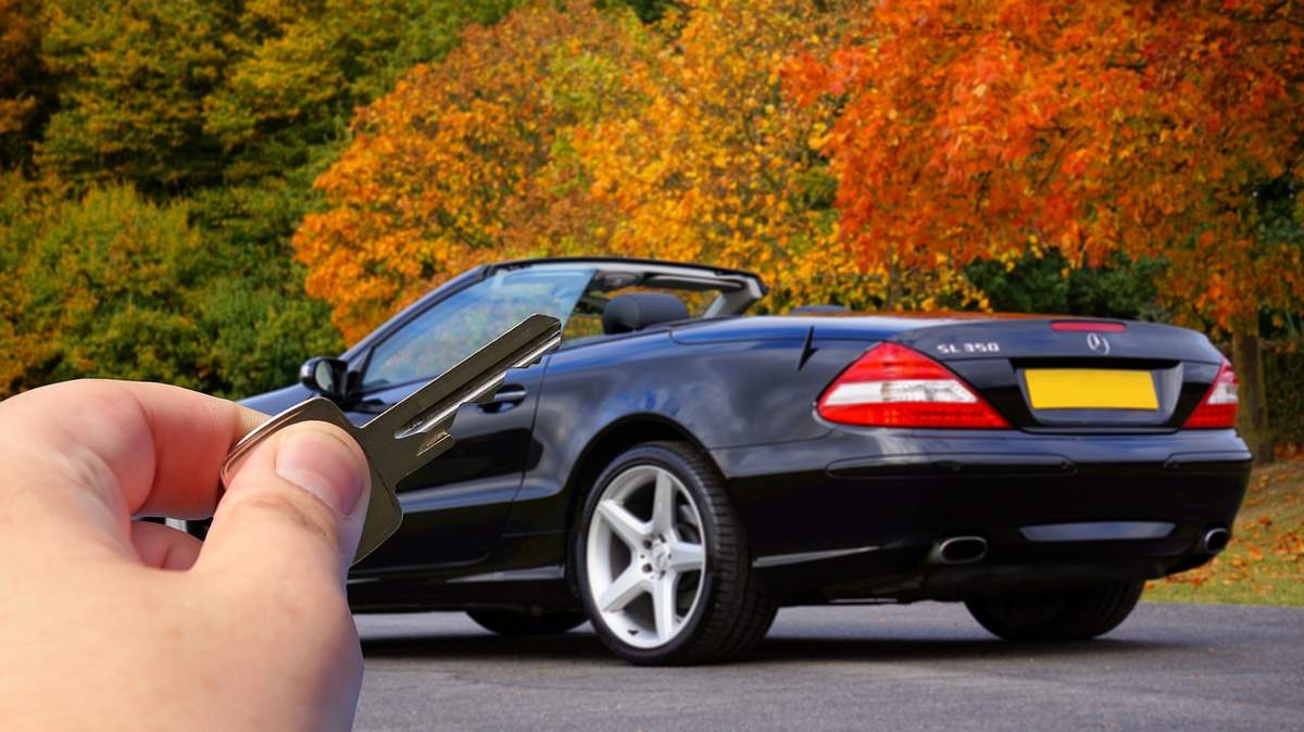 Une main montre des clés devant une voiture de sport noire
