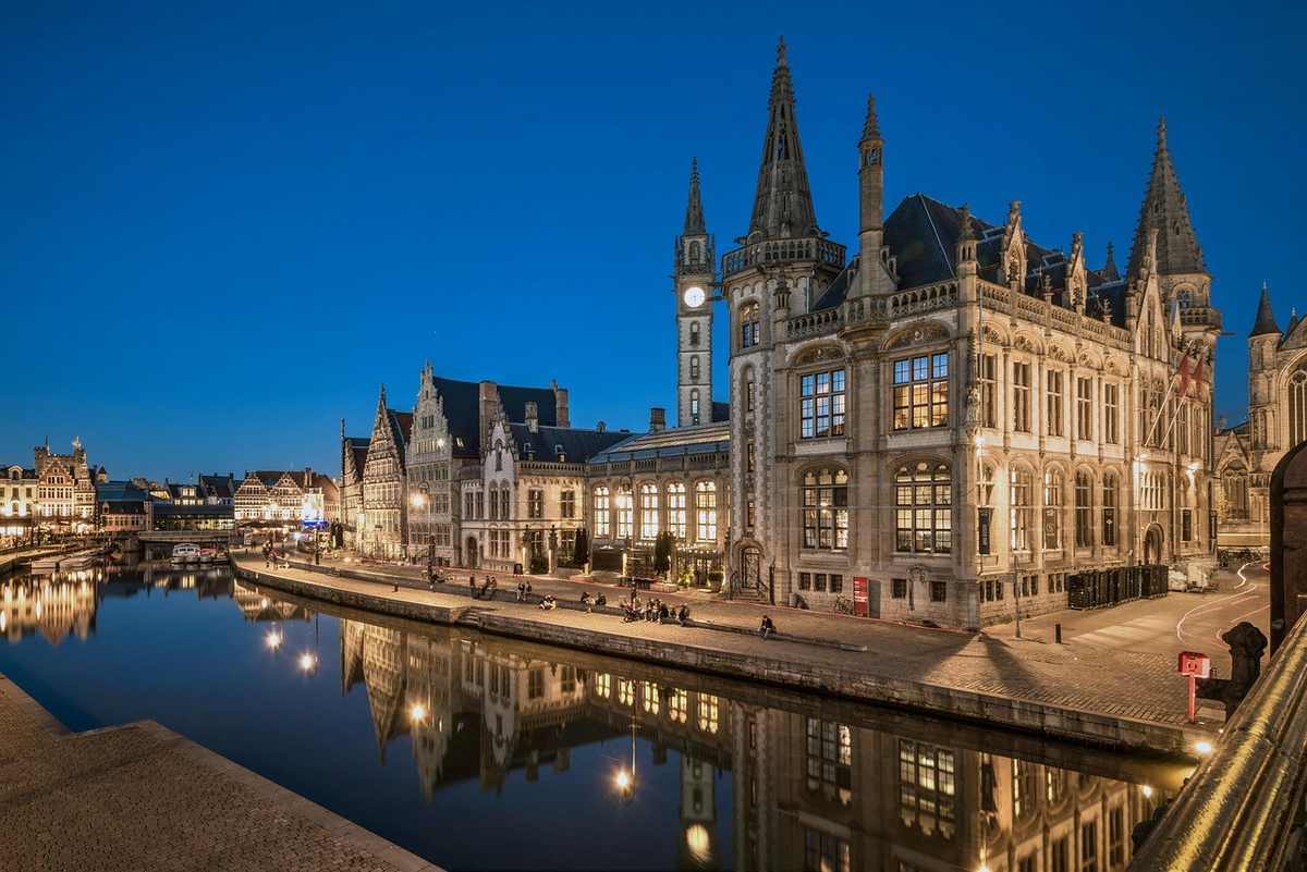 Bâtiment gothique majestueux illuminé sur les rives d'un canal tranquille sous le ciel nocturne