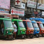 Des rickshaws colorés stationnés devant des boutiques et panneaux publicitaires