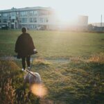Personne et chien marchant dans un champ avec un bâtiment en arrière-plan