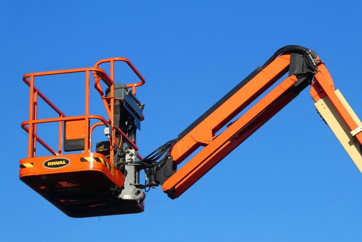 Plateforme orange élévatrice sur bras articulé contre ciel bleu Plateforme orange élévatrice sur bras articulé contre ciel bleu