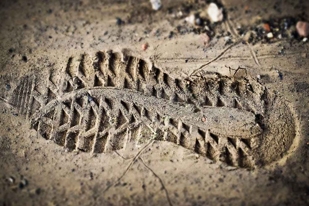 Empreinte de pied dans la boue, entourée de cailloux et de brindilles