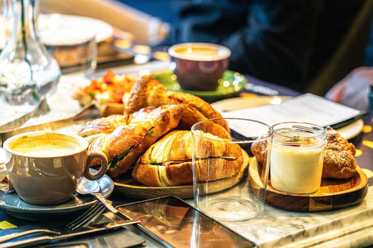 Table de petit-déjeuner avec café, pâtisseries, fruits, serviettes et couverts Table de petit-déjeuner avec café, pâtisseries, fruits, serviettes et couverts