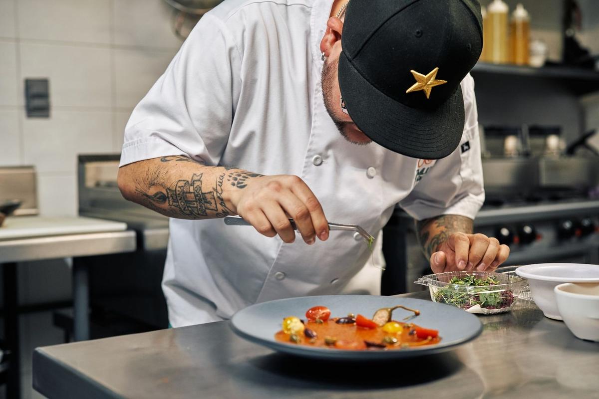 Chef tatoué garnissant une assiette de soupe dans une cuisine professionnelle Chef tatoué garnissant une assiette de soupe dans une cuisine professionnelle