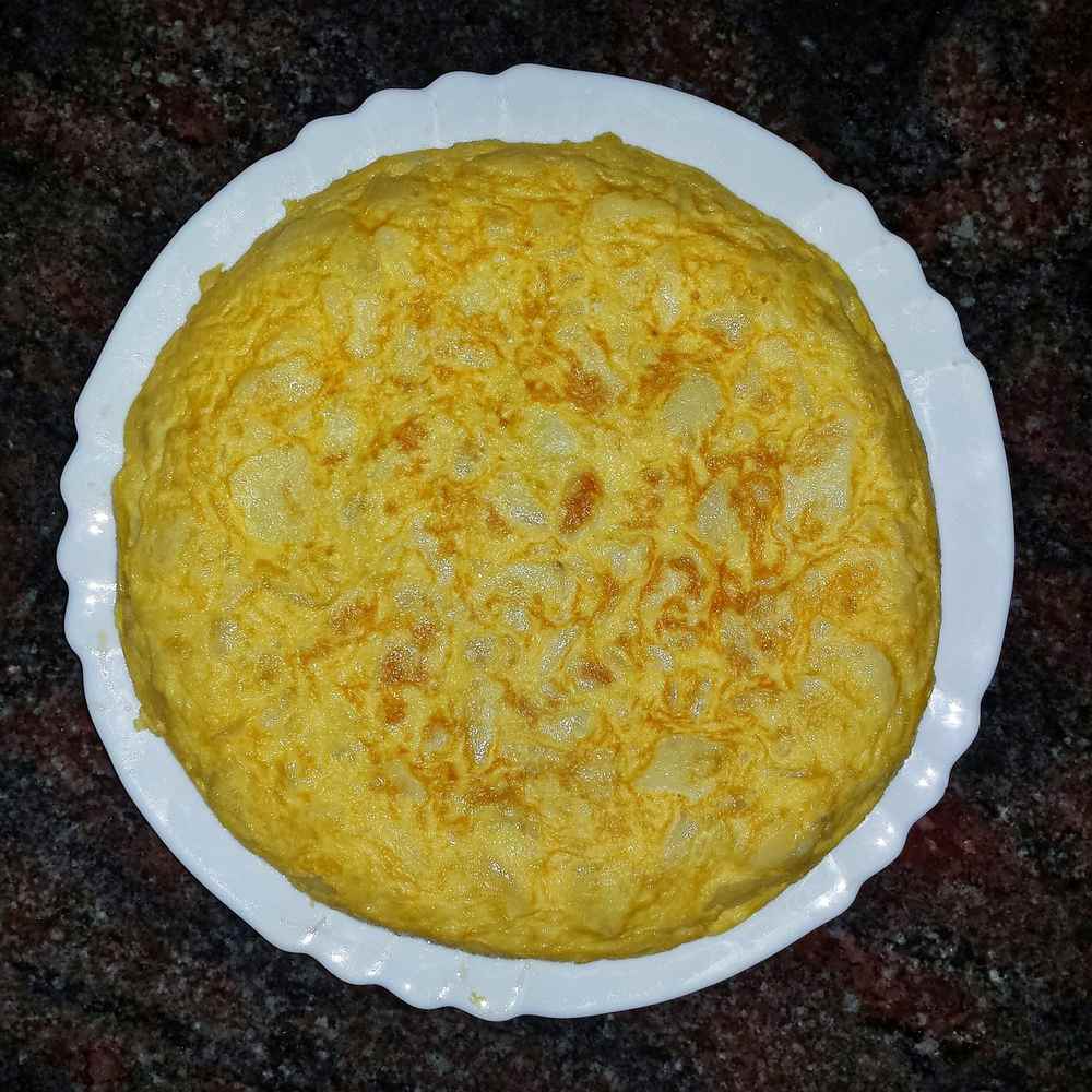 Tortilla espagnole dorée sur assiette blanche, plan de travail sombre