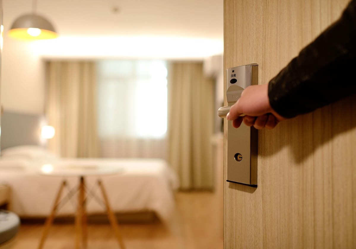 Une main ouvre la serrure d'une porte d'hôtel, chambre meublée derrière Une main ouvre la serrure d'une porte d'hôtel, chambre meublée derrière